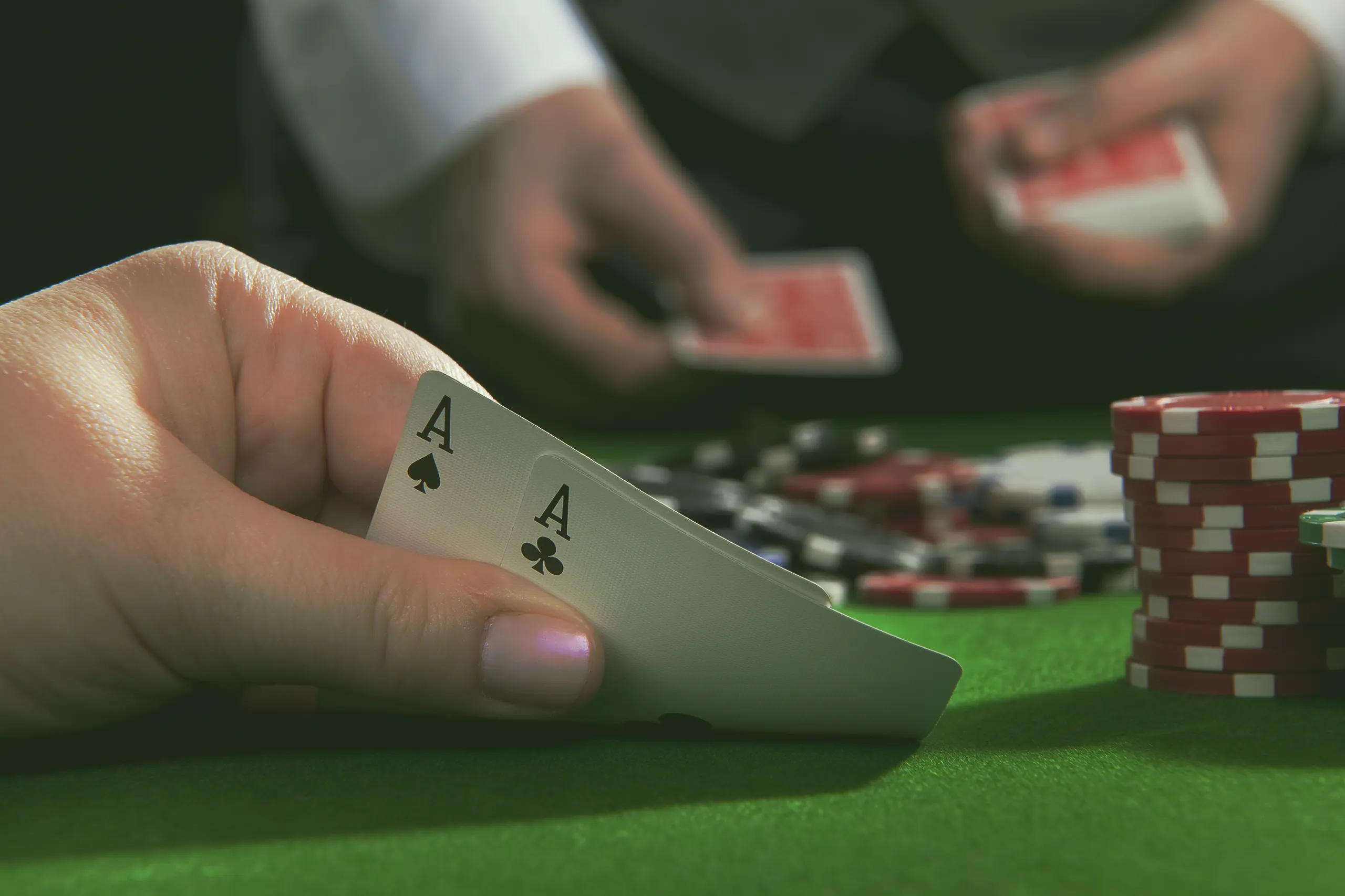 Starke Pokerhand mit Assen und Jetons im Casino Pokerhand mit zwei Assen auf grünem Filztisch, im Hintergrund ein Dealer mit Karten und ein Stapel Spielchips.